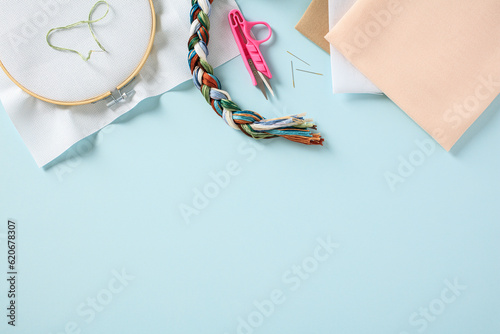 Embroidery hoop with blank canvas and needlework accessories on pastel blue background