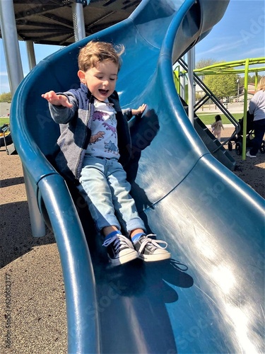 Action shot of toddler boy having fun going down a blue sliding board.