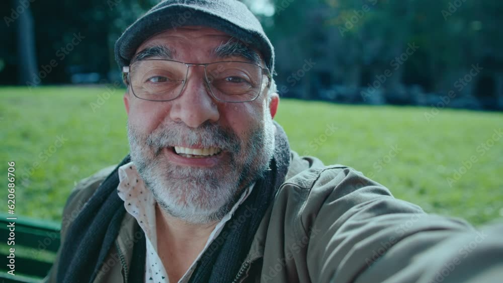 Cheerful senior man with gray beard looking at camera, speaking and showing thumb up, making a video call outdoors in the park. POV shot Cheerful senior man with gray beard looking at camera, speaking and showing thumb up, making a video call outdoors in the park. POV shot