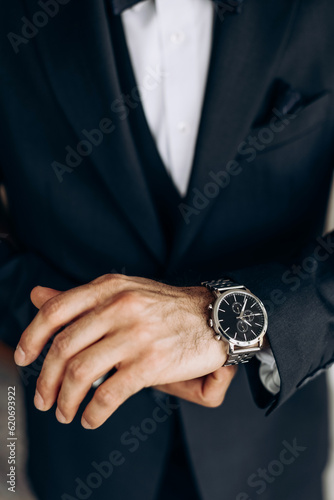 The man is dressed in a classic suit and an expensive wrist watch. Close-up of a mechanical watch on a man's hand. The concept of punctuality and confidence. A man puts on his wristwatch