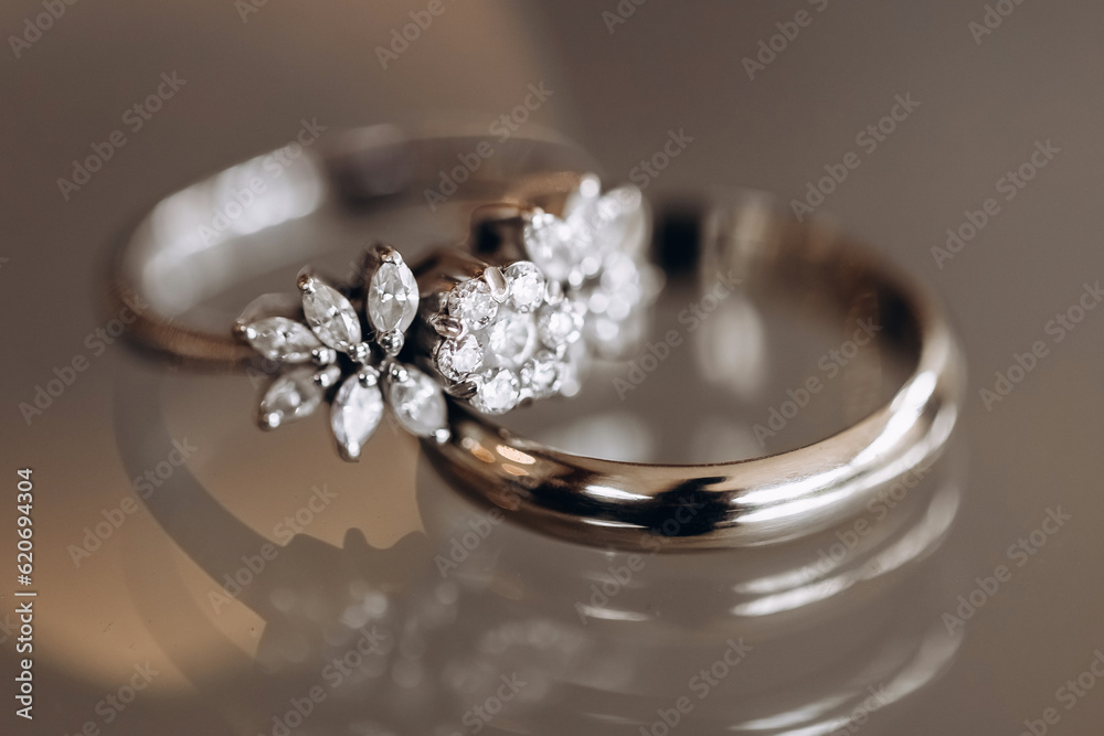 Wedding rings of the bride and groom with precious stones close-up. Wedding accessory in the form of gold rings with diamonds. Luxurious jewelry made of precious metals on a reflective surface Wedding rings of the bride and groom with precious stones close-up. Wedding accessory in the form of gold rings with diamonds. Luxurious jewelry made of precious metals on a reflective surface
