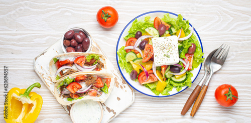 Traditional Greek Food: Greek Salad, Gyros with meat and vegetables, Tzatziki sauce, Olives on White rustic wooden table background top view. Cuisine of Greece