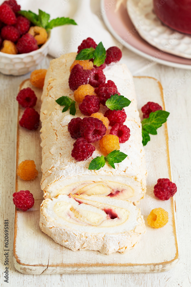 Meringue roll with butter cream and raspberry curd, decorated with berries on a light background.