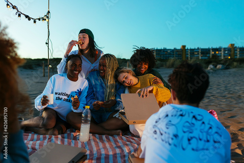 Happy diverse friends eating pizza on beach at evening