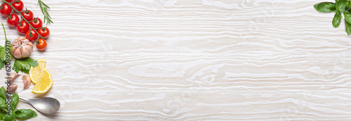 Healthy food ingredients composition with fresh cherry tomatoes, herbs, garlic cloves, lemon wedges and spoon on white wooden rustic background, overhead shot with copy space, long banner