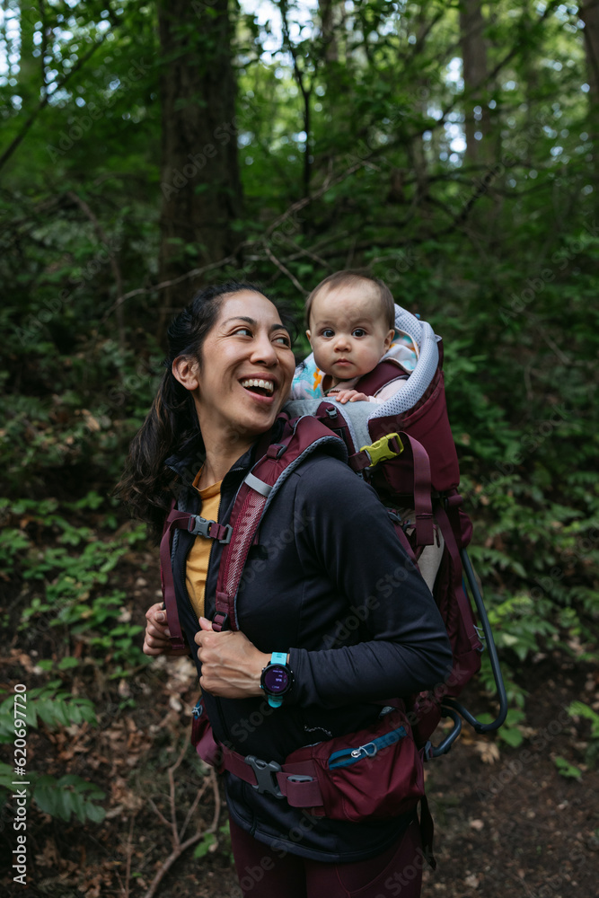 Smiling woman and baby in carrier outside in forest. Smiling woman and baby in carrier outside in forest.