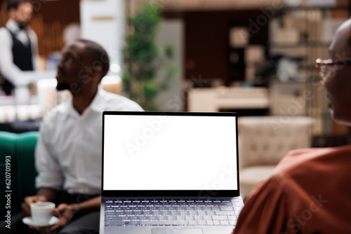 Tourist using white screen on pc sitting in lounge area at hotel lobby, checking blank copyspace with chroma key. Female guest holding laptop with isolated display at resort reception.