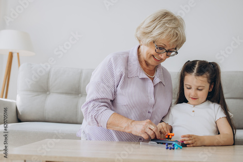 Grandmother playing a board game with granddaughter, sitting in the living room, smiling while having a great time together.