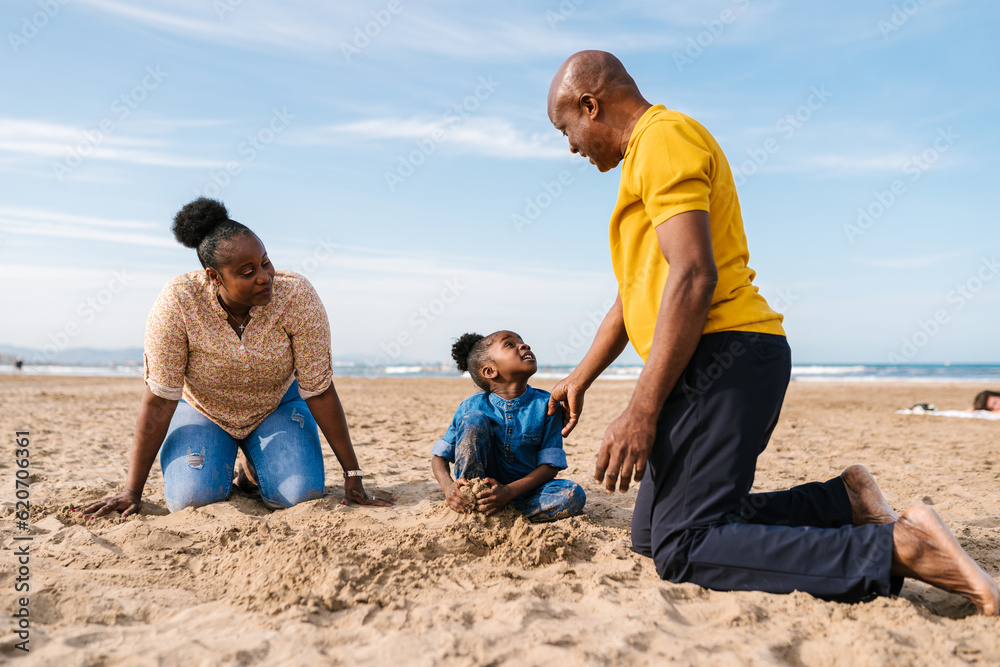 Black family and daughter playing with sand at beach