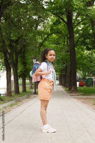 Adorable schoolkid standing on alley in city park
