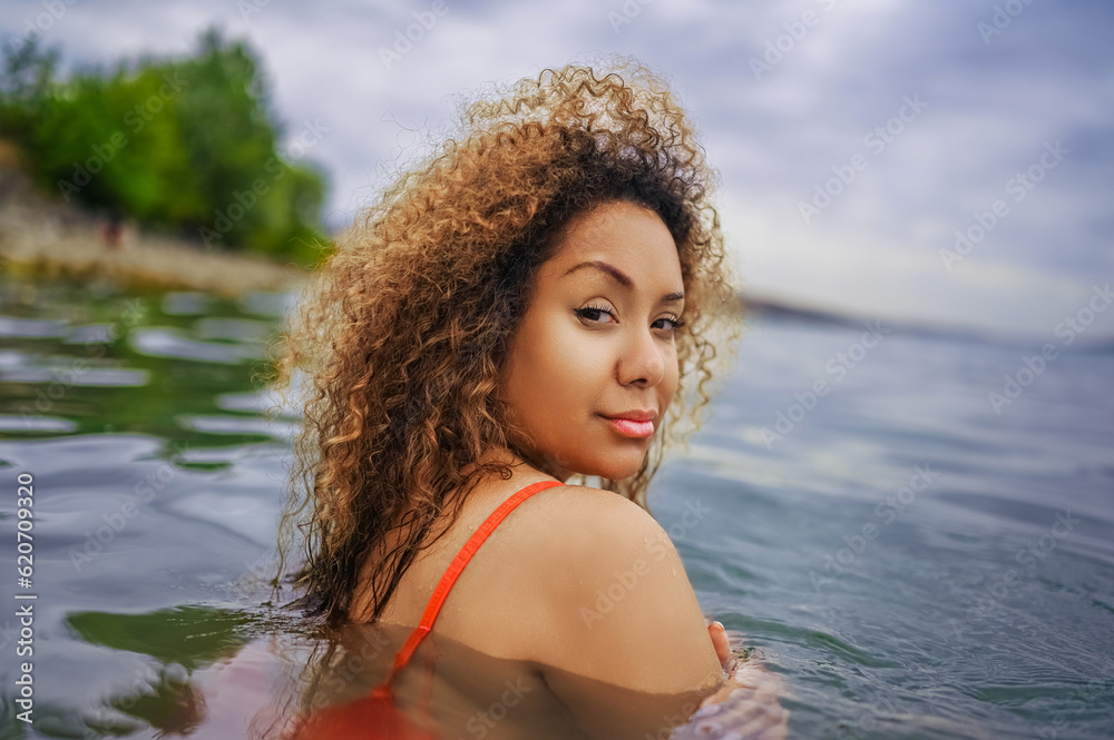 Attractive happy plus size African American Black woman enjoys swimming having fun with water splashes in sea lake water in cloudy weather outdoor