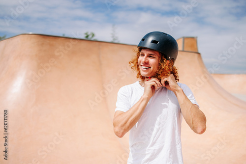 Smiling curly ginger hair skater boy putting her helmet on  photo
