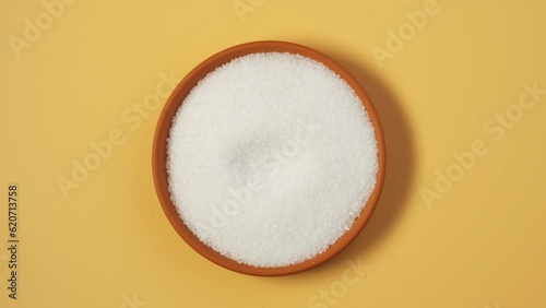 Tartaric acid powder in plate on yellow background. Video 4K. Rotating, clockwise. Food additive E 334. Acidity regulator, antioxidant synergist, complexing agent. White crystalline organic acid. photo