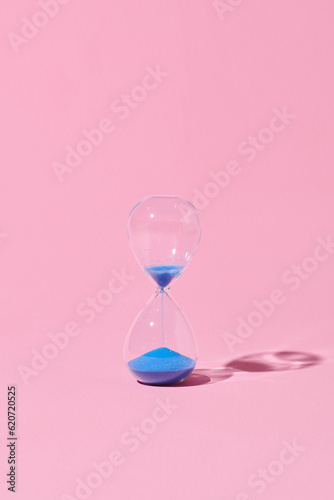Hourglass with blue sand on pink background. photo