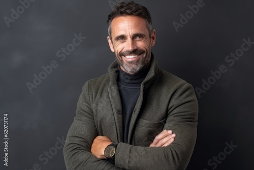 Portrait of a handsome mature man smiling at the camera while standing with crossed arms against black background