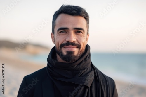 Portrait of handsome bearded man in black scarf looking at camera on the beach