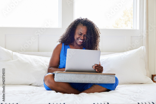 Happy mature Black woman sitting in bed using computer lap desk photo