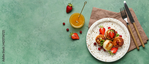 Plate with cottage cheese pancakes, berries and honey on green background with space for text