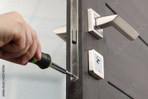 Handyman with screwdriver repairing door lock indoors, closeup