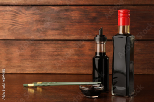 Bottles, bowl with soy sauce and chopsticks on wooden table. Space for text