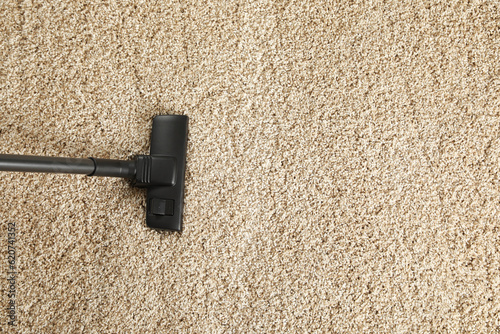 Hoovering beige carpet with modern vacuum cleaner, top view. Space for text