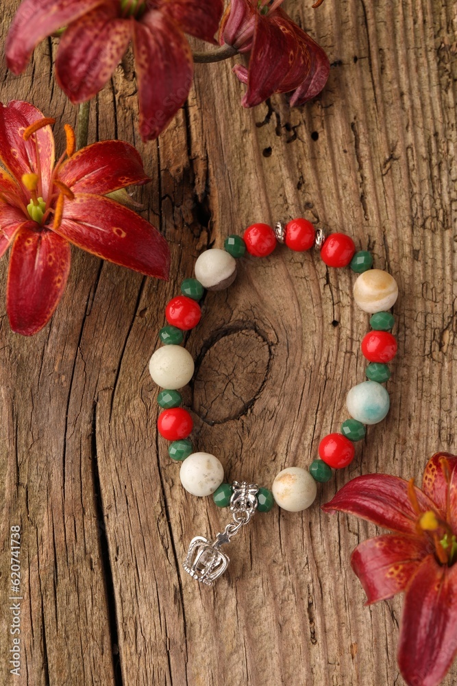 Beautiful bracelet with gemstones and lily flowers on wooden surface, flat lay