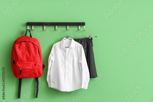 Stylish school uniform and backpack hanging on rack near green wall in room