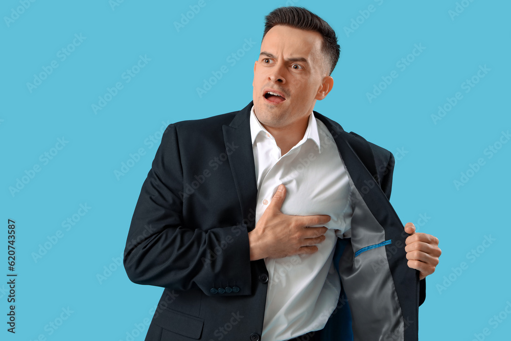 Young businessman having heart attack on blue background Young businessman having heart attack on blue background