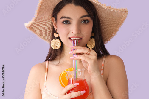 Young woman drinking summer cocktail on lilac background, closeup