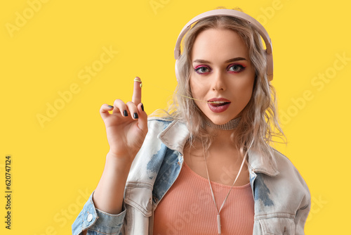 Obraz na plátně Young woman in headphones chewing gum on yellow background