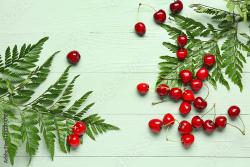 Many sweet cherries and leaves on green wooden background