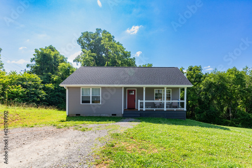 building exterior of grey home with red door, gravel drivewat and blue skies