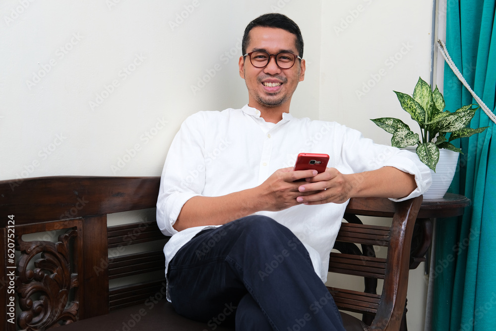 A man sitting relax on a couch holding mobile phone with happy expression