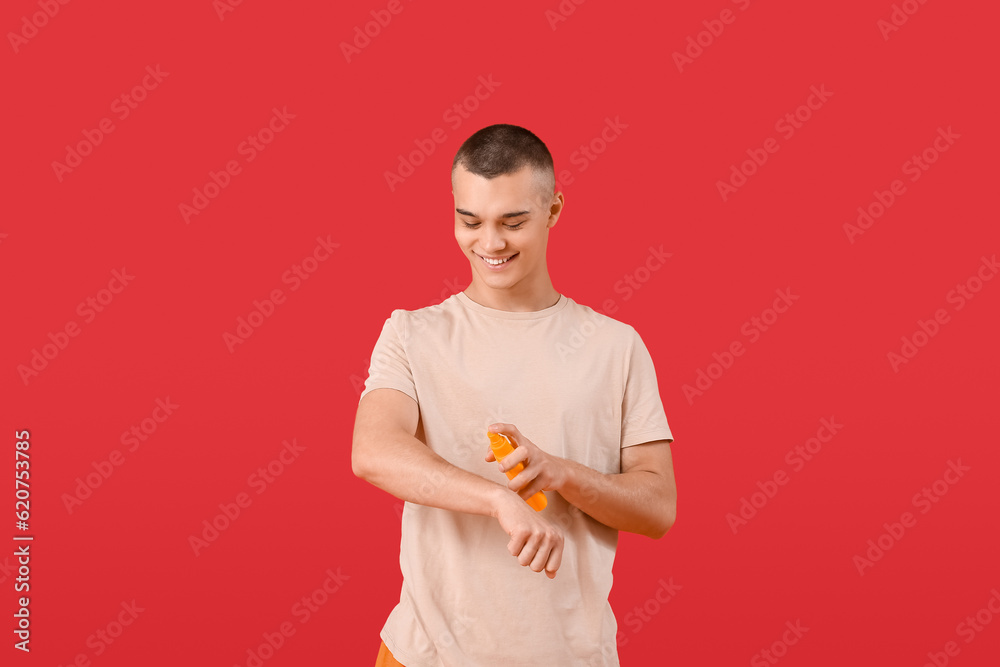 Happy young man applying sunscreen cream on his body against red background Happy young man applying sunscreen cream on his body against red background