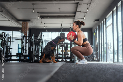 Cheerful Asian woman exercising by lifting weights in gym with puppies.