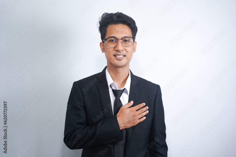 Young Asian man wearing suit smiling while holding hands on his chest Young Asian man wearing suit smiling while holding hands on his chest