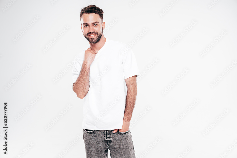 Fototapeta premium Portrait of handsome smiling stylish hipster lambersexual model. Sexy man dressed in white T-shirt and jeans. Fashion male isolated on white background in studio