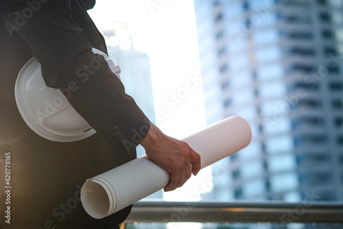 An engineer holds a building plan and is working and supervising the construction, he is reading plans for production, business and investment.