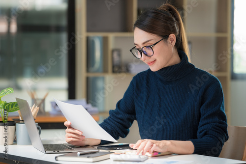 Portrait of businesswoman accountant using calculator and laptop for matching financial data saving in office room, Business financial, tax, accounting concept