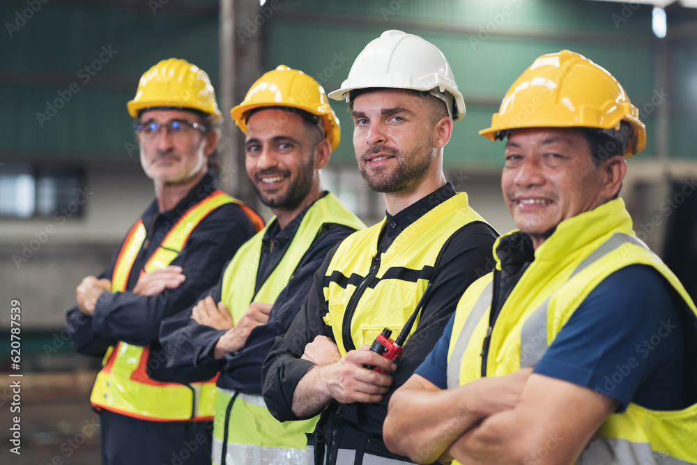 Group of male factory workers standing together with crossed arms and smiling in industry factory, wearing safety uniform and helmet. Factory workers working in factory Group of male factory workers standing together with crossed arms and smiling in industry factory, wearing safety uniform and helmet. Factory workers working in factory