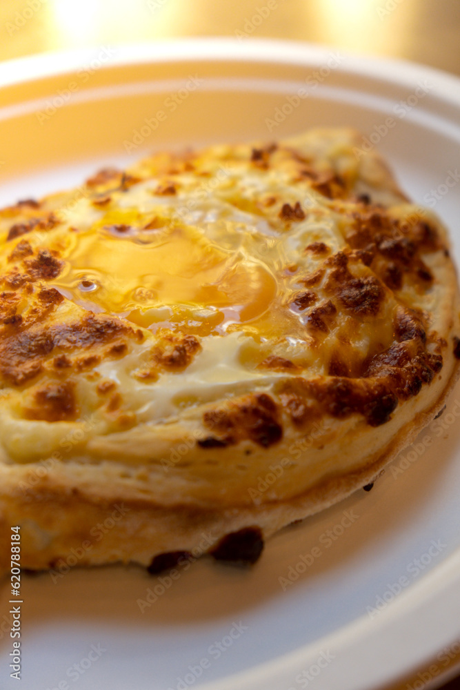 Traditional Georgian cuisine. Ajara khachapuri on paper plate. Filled with cheese and topped with raw egg and butter, cheese-filled bread. Delicious food Traditional Georgian cuisine. Ajara khachapuri on paper plate. Filled with cheese and topped with raw egg and butter, cheese-filled bread. Delicious food