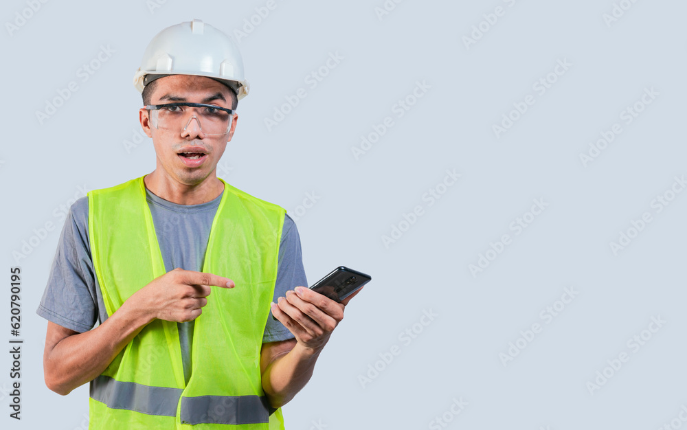 Amazed engineer using cell phone. Impressed engineer pointing finger at mobile phone. Young engineer holding cell phone on isolated background Amazed engineer using cell phone. Impressed engineer pointing finger at mobile phone. Young engineer holding cell phone on isolated background
