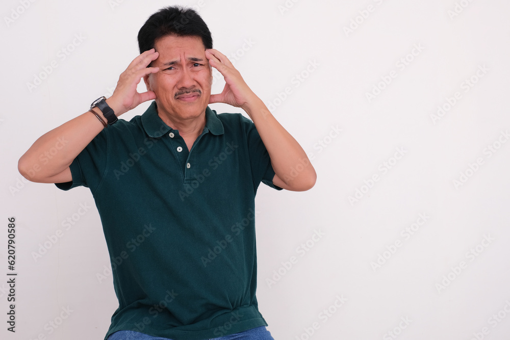 Man in casual clothes sitting and pressing his forehead with both hands, looking sick Man in casual clothes sitting and pressing his forehead with both hands, looking sick