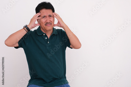 Man in casual clothes sitting and pressing his forehead with both hands, looking sick