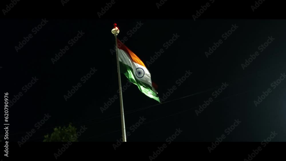 Indian tri colour national flag hoisted on a tall poll in front of a indian railwaystation at night.