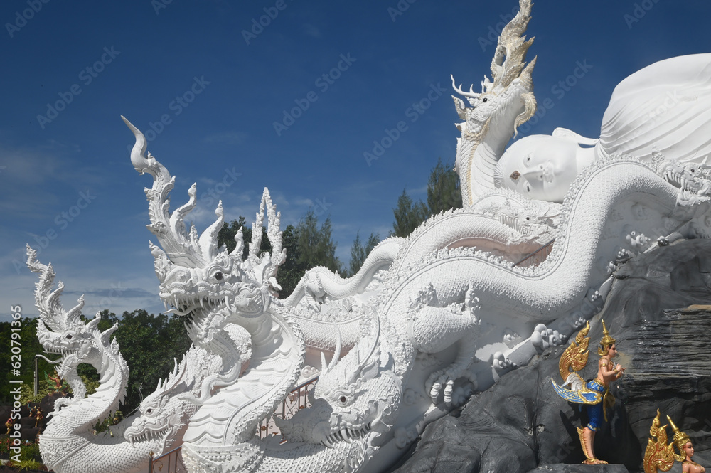 Fototapeta premium Large white outdoor reclining Buddha enshrined under the protection of the Serpent at Wat Don Khanak for peoples travel to pay homage to the holy things. Located at Nakhon Pathom Province in Thailand