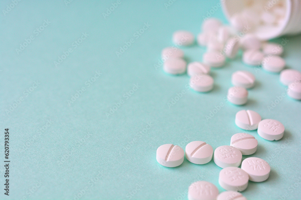 水色の背景に散らばる複数の白い錠剤と薬のボトル 水色の背景に散らばる複数の白い錠剤と薬のボトル
