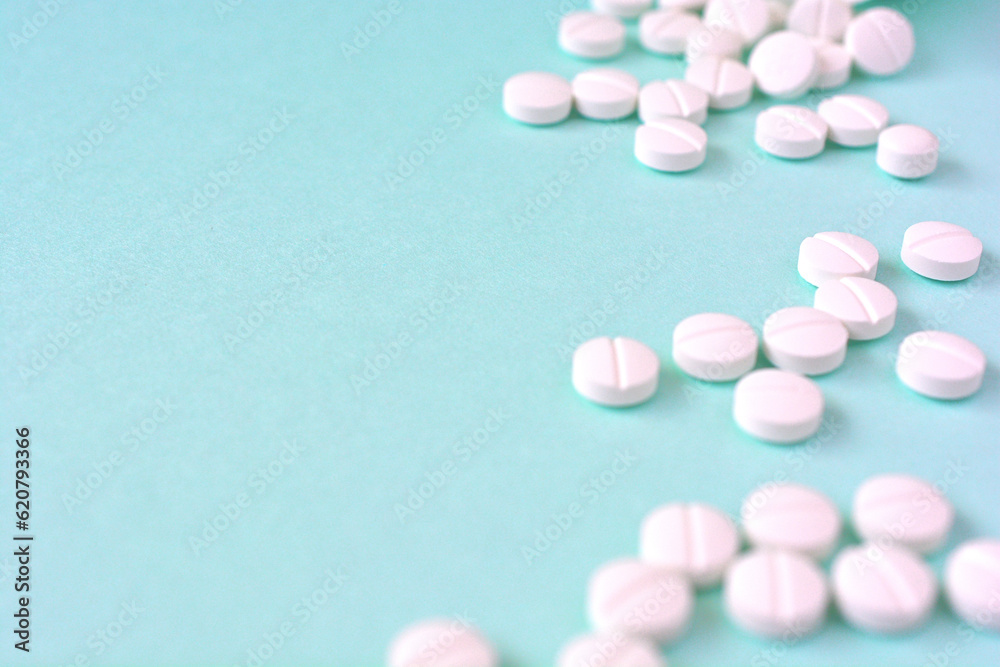 水色の背景に散らばる複数の白い錠剤と薬のボトル