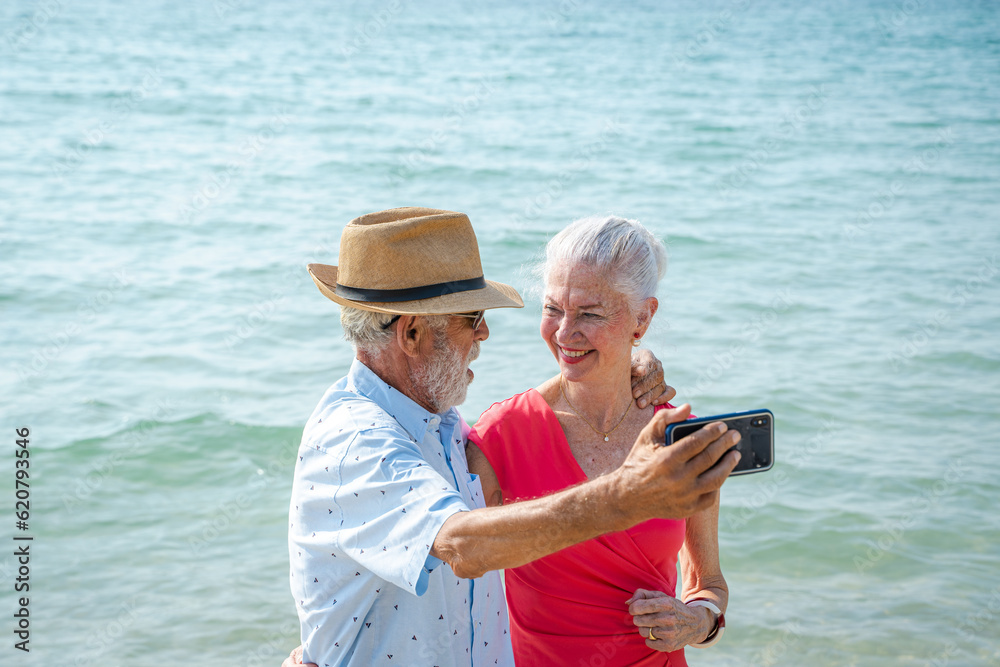 Mature couple taking pictures together by the sea during summer seaside trip,Happy retirement,Ocean and outdoor embrace with love.