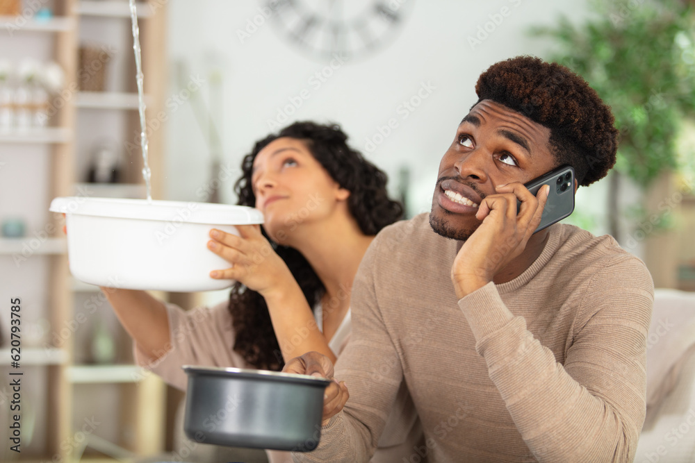 young couple collecting water in bucket from ceiling in house Stock